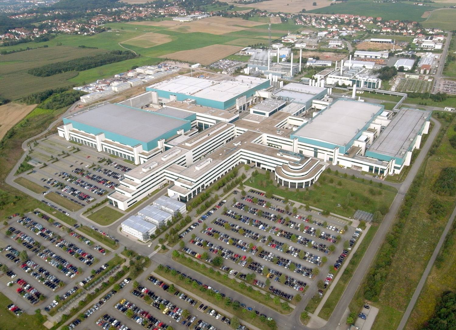Aerial view of GlobalFoundries Fab 1 in Dresden: large white and teal cleanroom buildings surrounded by car parks and fields