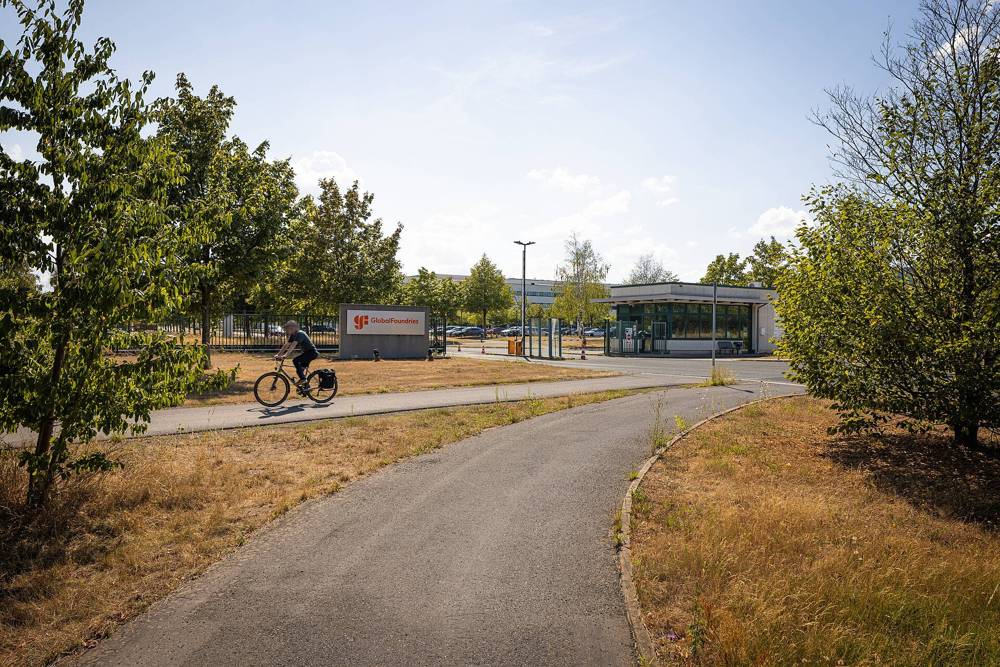 Cyclist on a path in front of the GlobalFoundries entrance sign and gatehouse in Dresden
